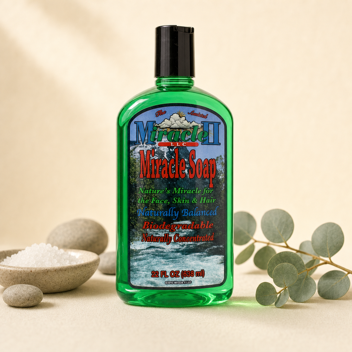 Miracle II Miracle Soap 22 fl oz green bottle on a warm cream background with river stones, mineral salt and eucalyptus